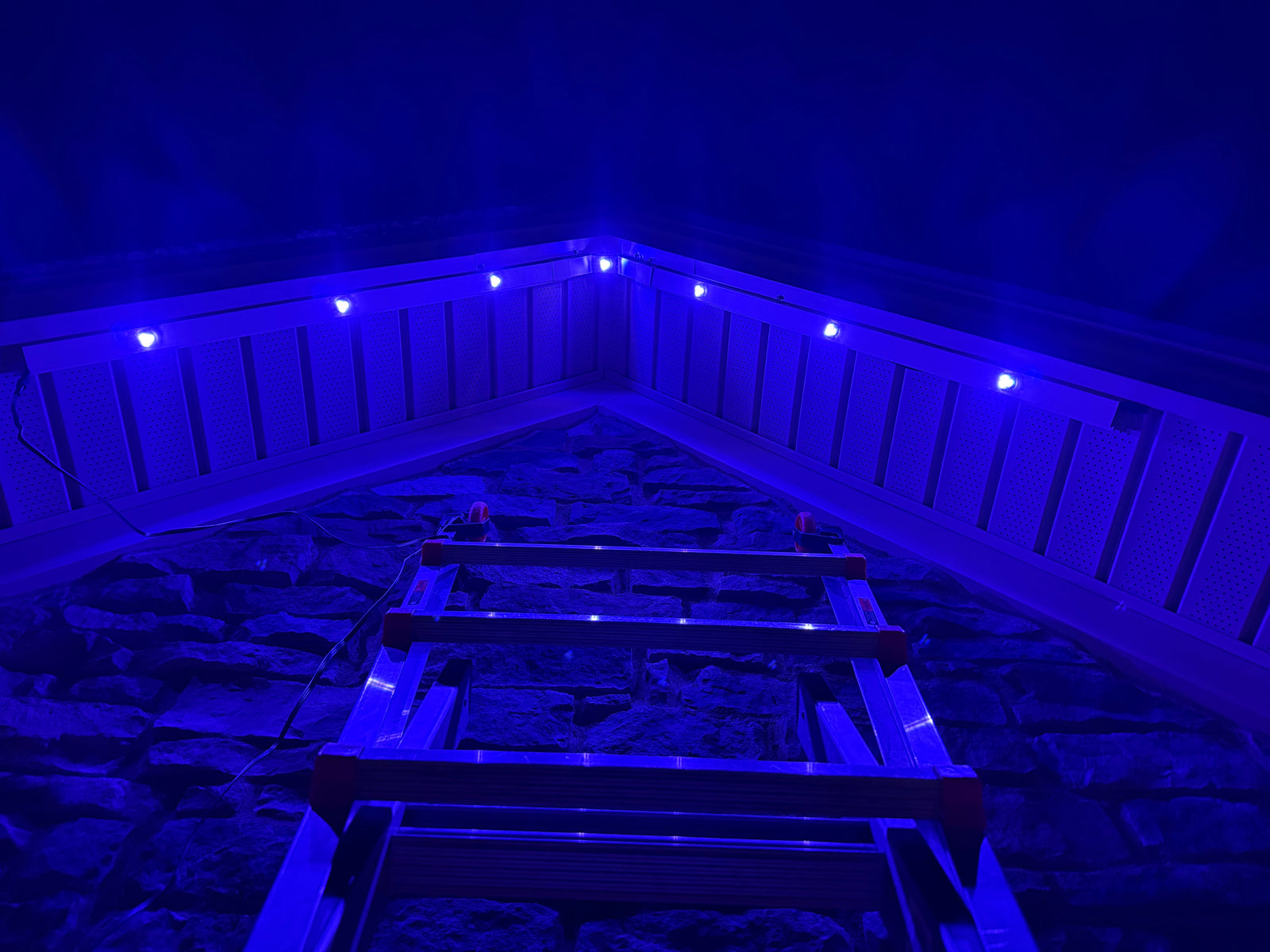 Looking up a ladder at a gable glowing electric blue, mid-install